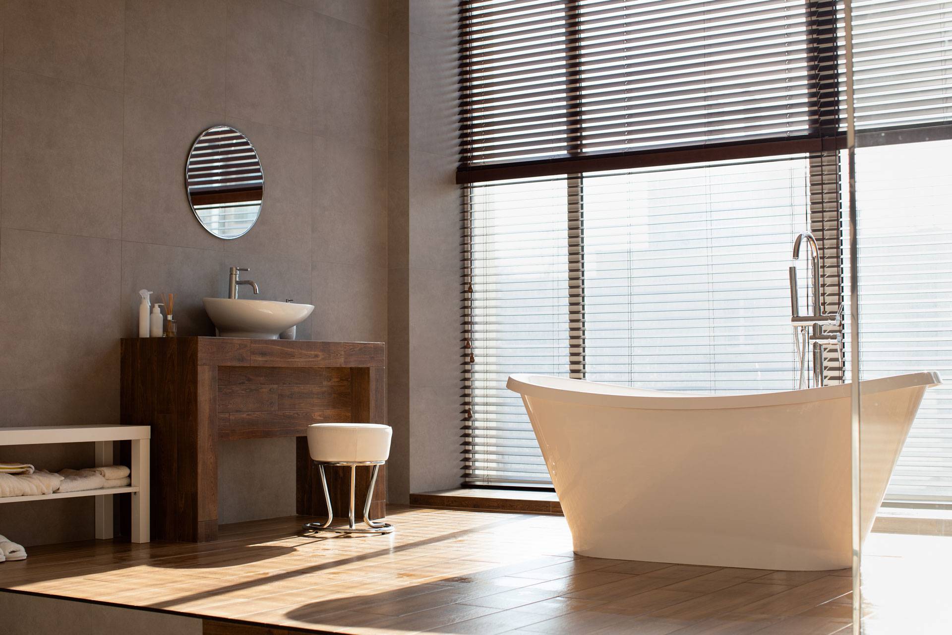 Salle de bain design avec baignoire îlot, vasque en bois et grande baie vitrée avec stores
